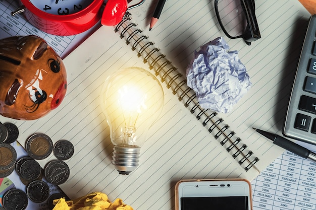 Posto di lavoro e lampadina di vista superiore sul libro con gli articoli per ufficio intorno nel concetto dell'ufficio