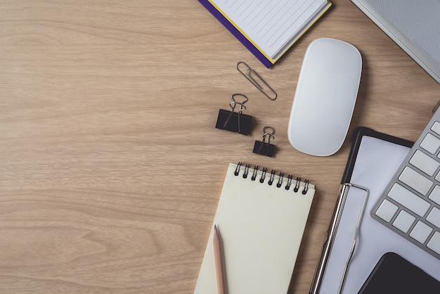 Top view of workspace with diary or notebook and clipboard, laptop, mouse computer, keyboard, smart phone, pencil, pen on wooden background