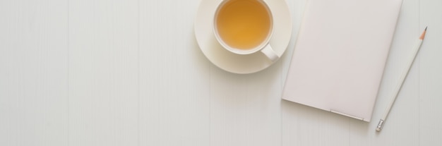 Top view of workspace with diary notebook, pencil, tea cup and copy space on plank table