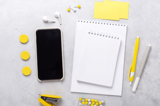 Top view of workspace with smartphone, notepad and stationery accessories on gray stone background. Illuminating Yellow and Ultimate Gray, colors of the year 2021 - Image