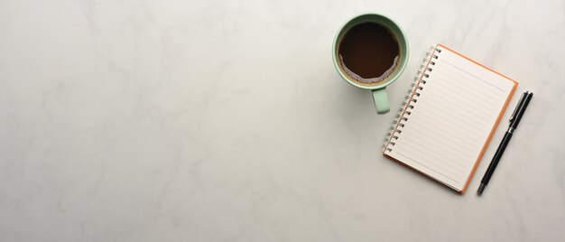 Top view of worktable with notebook, pen, coffee cup and copy space on marble desk