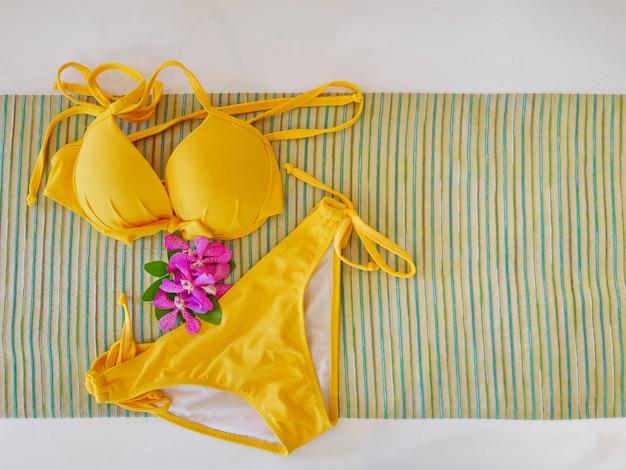 Photo top view of yellow bikini with purple orchid on abstract fabric