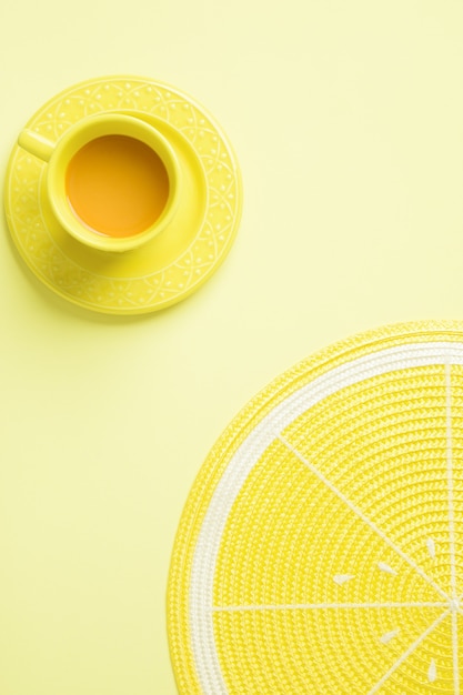 Top view of a yellow cup of tea and a lemon placemat on yellow