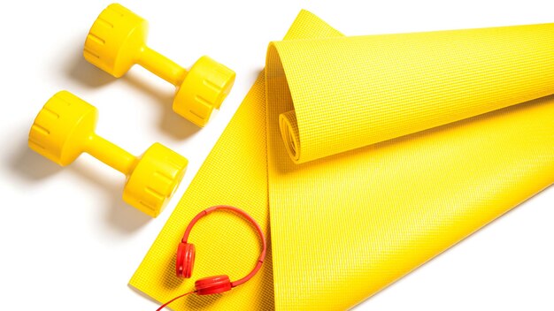 Top view of yellow dumbbells, fitness mat and red headphones on white background