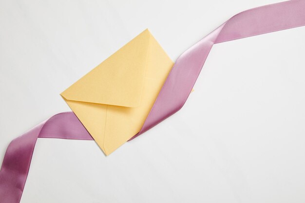 Вид сверху на желтый конверт и фиолетовую атласную ленту на белом