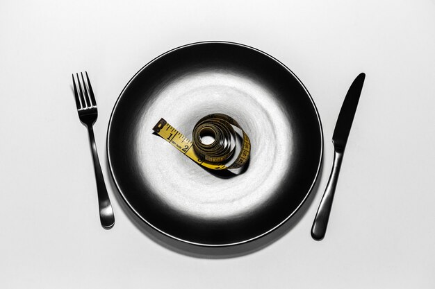 Top view of yellow measuring tape on black plate with knife and fork isolated