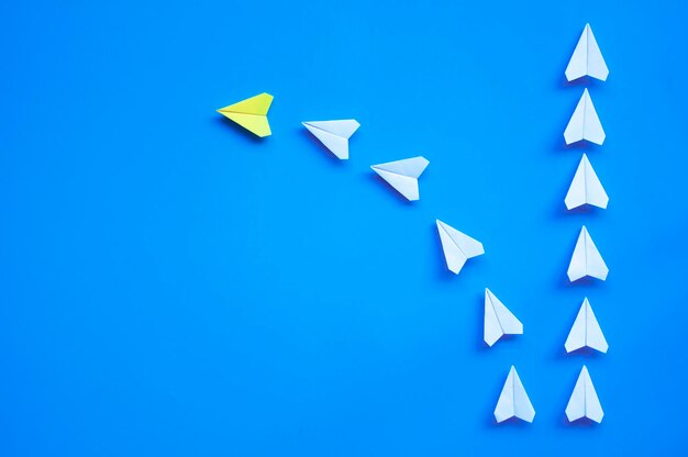 Top view of yellow paper airplane origami leading other white airplanes on blue background with customizable space for text or ideas leadership skills concept and copy space