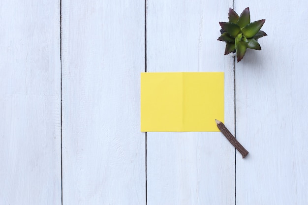 La carta gialla di vista superiore, la matita ed il vaso di fiore sul pavimento di legno bianco e hanno lo spazio della copia. Foto Premium