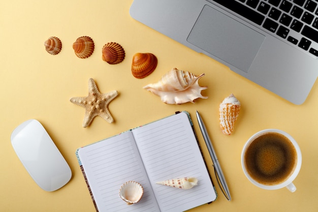 Top view yellow table open notebook cup of coffee mouse pen shells. Travel vacation concept. Dreaming about vacation on a tropical beach.