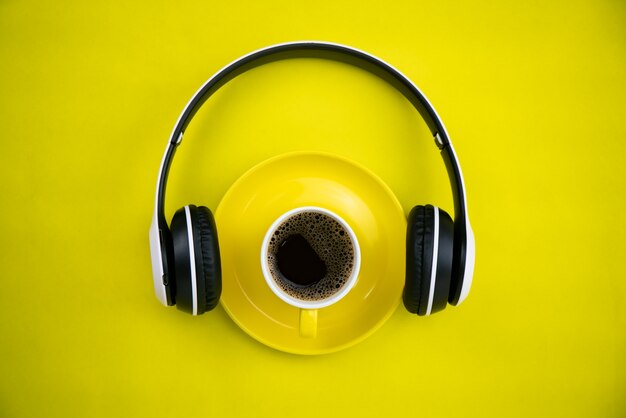 Foto vista dall'alto della tazza di caffè yellpw con le cuffie su sfondo di carta gialla.