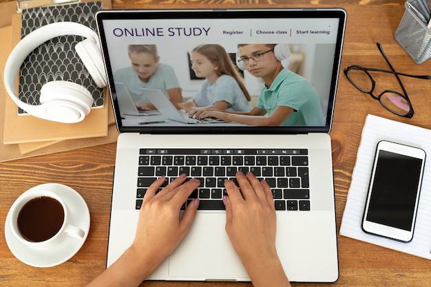 Top view of young adult hands typing on laptop keypad surrounded by business supplies