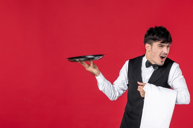 Top view of young concerned man waiter in a uniform with bow tie holding tray and towel