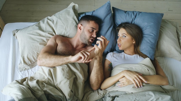 Top view of young couple lying in bed upset and argue each other