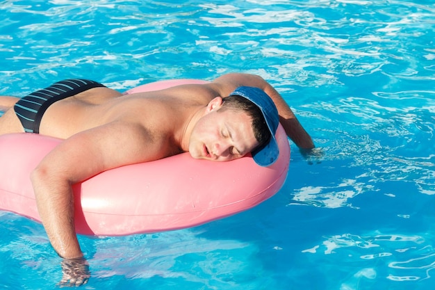 Photo top view of young drunk guy swim with pink circle in pool drunk guy on vacation in the hotel