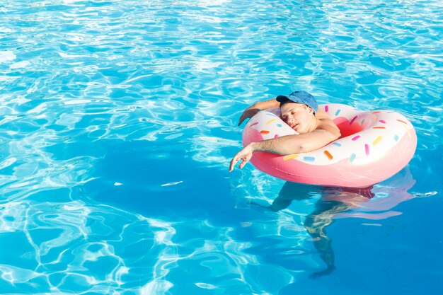 Top view of young drunk guy swim with pink circle in pool.