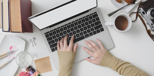 Top view of young female typing on laptop computer in cozy workspace with office supplies 