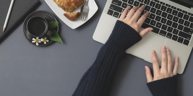 Top view of young female typing on laptop computer in winter workspace with office supplies 