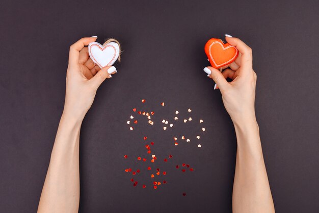 Top view of young girl's hands are holding red and white hearts. around candy from red hearts. Grey background. Valentine's Day.