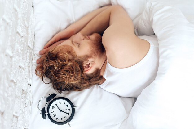 Top view. Young hipster sleeps under white blanket