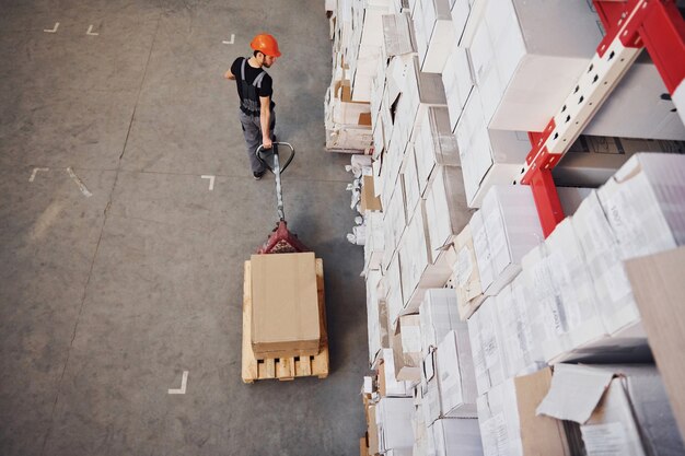 Top view of young male worker in uniform that is in the warehouse pushing pallet truck.