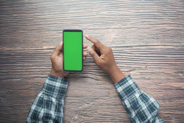 Top view of young man hand using smart phone with green screen on table