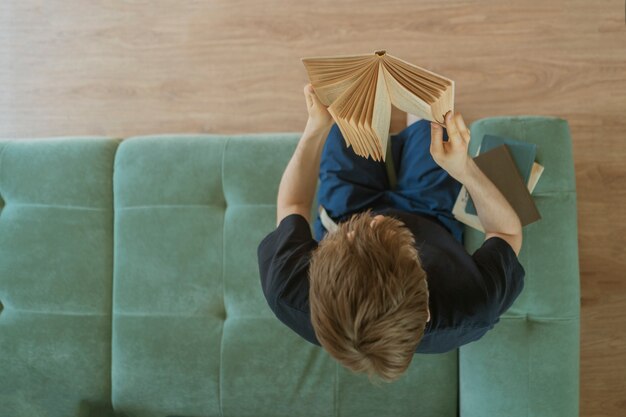 A top view of young man sitting on the wooden floor and reading the book at home