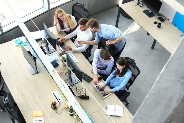 Vista dall'alto di giovani colleghi moderni in abbigliamento casual intelligente che lavorano insieme mentre trascorrono del tempo in ufficio.