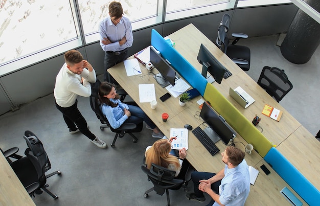 Top view of young modern colleagues in smart casual wear working together while spending time in the office