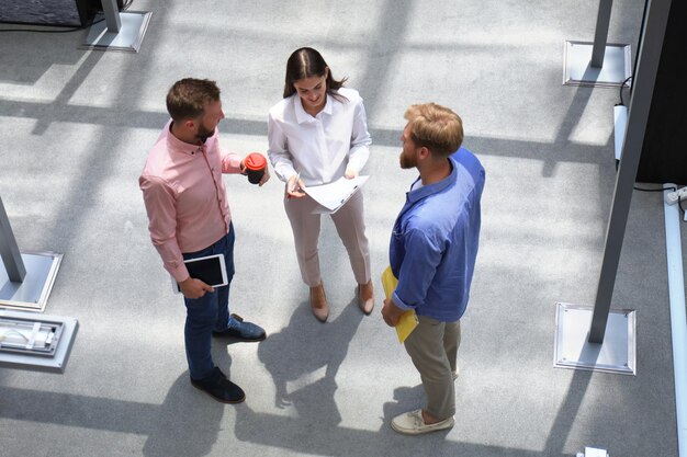 Top view of young modern people in smart casual wear discussing business while standing in creative office