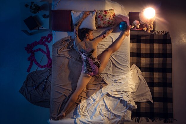 Top view of young professional rhythmic gymnast sleeping at her bedroom in sportwear with ribbon.