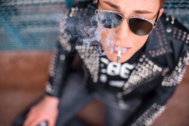 Top view of a young stylish man wearing sunglasses is smoking a cigarette