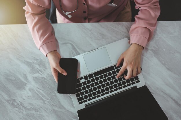 Top view of a young woman doctor with a gray computer sitting on the soft and white floor of the bed