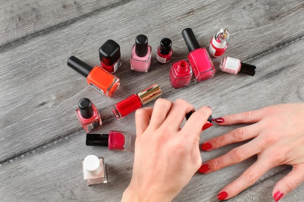Top view - young woman hands, applying second layer of nail varnish, with more bottles of polish in back, on gray wood desk. All trademarks blurred/cloned out.