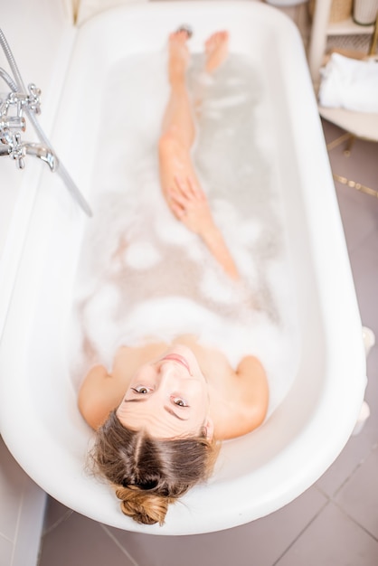 Top view on the young woman lying in the bath full of foam