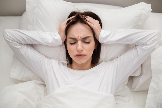Top view of young woman lying in bed touching head