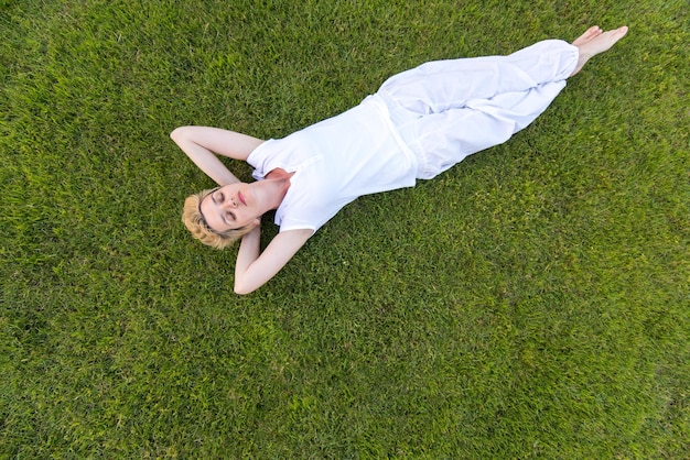top view of young woman relaxing on the grass while lying down with hands behind head, relaxation and nature concept