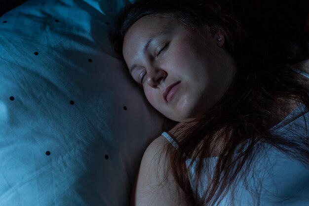 Vista dall'alto della giovane donna che dorme comodamente su un letto di notte, i colori notturni blu