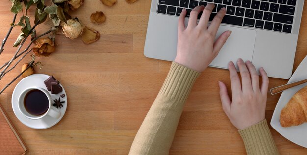 Top view of young woman typing on laptop computer in comfortable workplace with office supplies