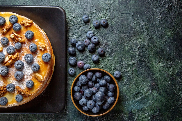 Top view yummy honey cake with blueberries and walnuts inside plate dark surface