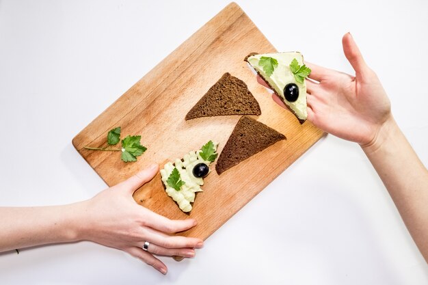 Top virew woman holding fresh avocado and making sandwiches on the table with other ingredients