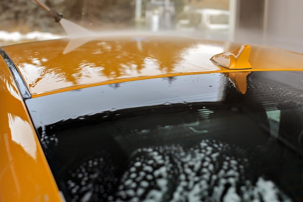 Top of yellow car washed in carwash, water flowing on roof and small antenna.