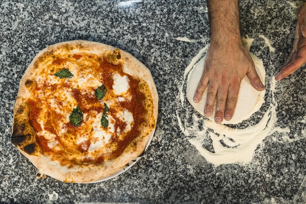 Topdown shot of hands preparing pizza dough next to prepared margherita pizza bakery