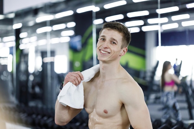 Топлесс молодой фитнес-мужчина с полотенцем ходит после тренировки в спортзале