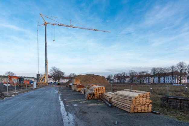 Torenkraan en graafmachine op een bouwterrein met gestapelde hout blauwe hemel met lichte wolken