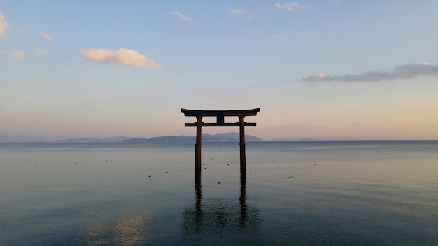 torii gate in calm lake against sky during sunset