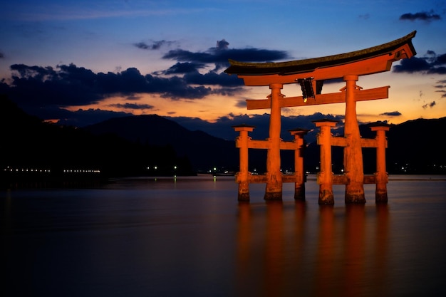 torii gate in lake against sky during sunset