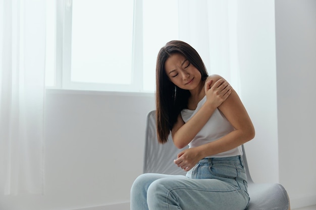 Tormented from shoulder dislocation fractures pain after\
lifting weights in the wrong position tanned beautiful young asian\
woman touching painful shoulder at home interior living room cool\
offer