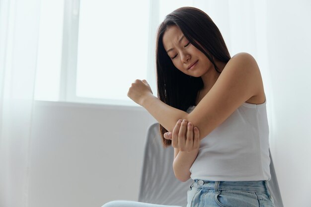 Tormented suffering tanned beautiful young asian woman hurting\
holding painful elbow at home interior living room injuries poor\
health illness concept cool offer banner