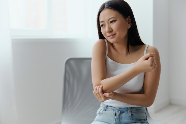 Tormented suffering tanned beautiful young asian woman hurting
holding painful elbow at home interior living room injuries poor
health illness concept cool offer banner