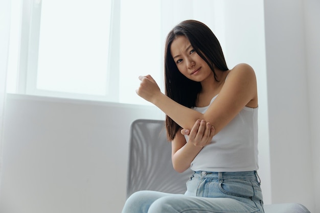 Tormented suffering tanned beautiful young asian woman hurting
holding painful elbow at home interior living room injuries poor
health illness concept cool offer banner